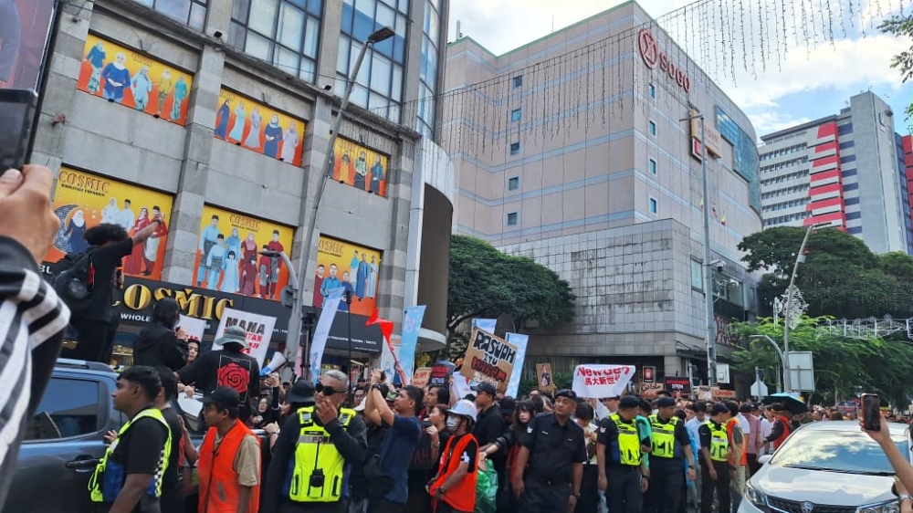 Marsyal perhimpunan yang memakai jaket oren bekerjasama dengan polis dengan jaket kuning untuk memastikan perarakan yang selamat dan teratur di sepanjang Jalan Tuanku Abdul Rahman di Kuala Lumpur. — Gambar oleh Ida Lim